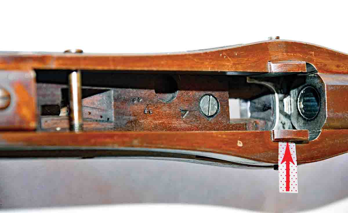 With the breechblock removed, you can see more of the genius in the design. To the left is the single takedown/pivot screw. The red arrow shows how the chocks fit into place. There is a short forcing cone in the rear of the barrel, and a sheet metal “apron” under the barrel and up the sides of the receiver that shields the wood from the escaping gas. The breechblock latch goes through the hole in the bottom where it locks everything into place.
